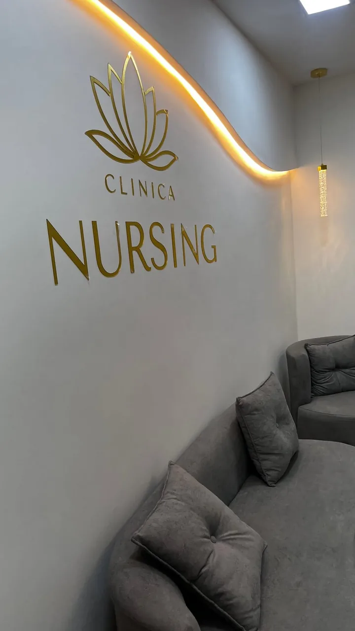 Recepção real da Clínica Nursing, com parede clara, iluminação quente e logotipo dourado